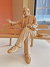 一个人的雕塑模型，他盘腿坐在长凳上，旁边是几本书
